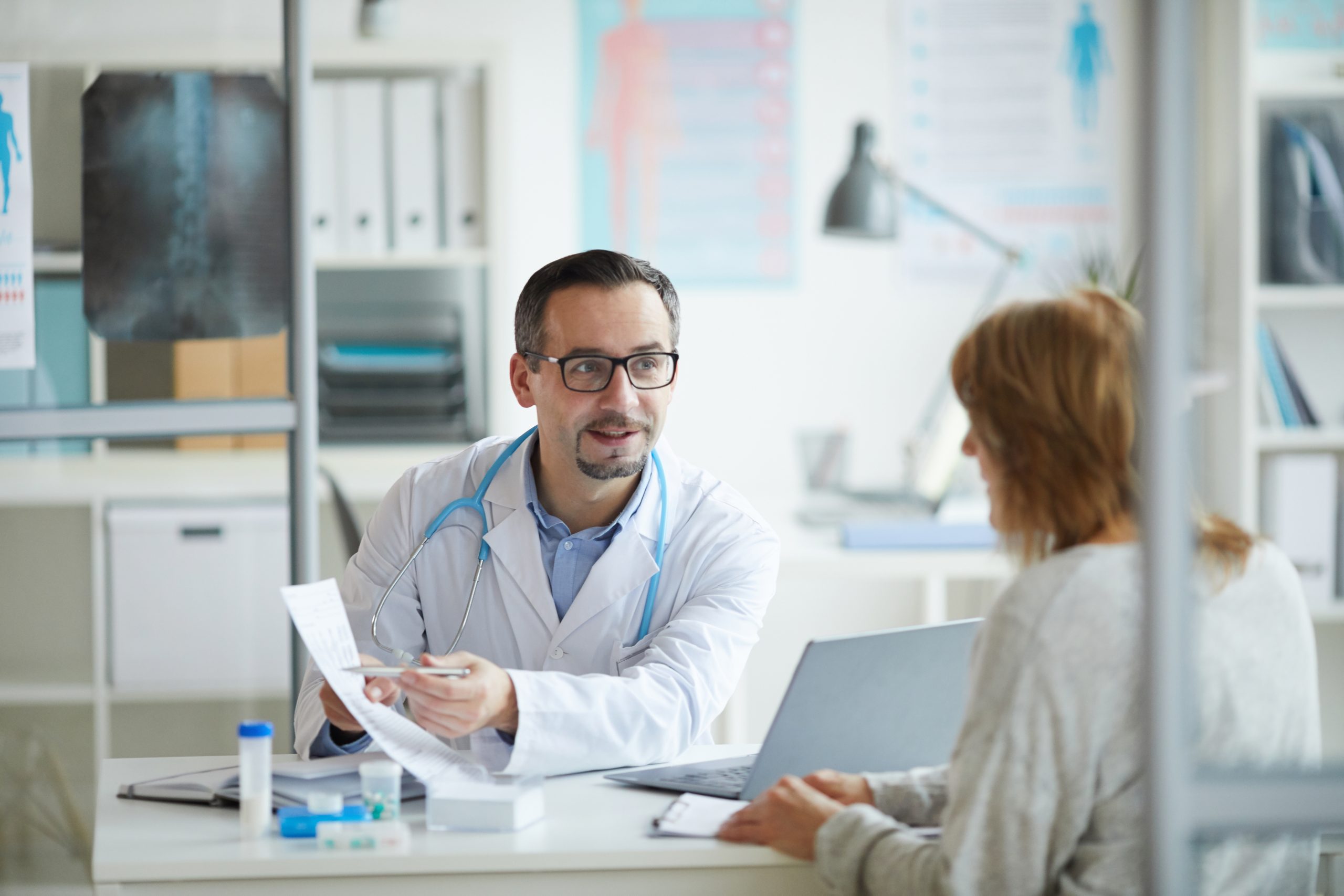 Doctor consulting his patient Mature healthcare worker showing some document to his patient and explaining the treatment for her while they sitting at office